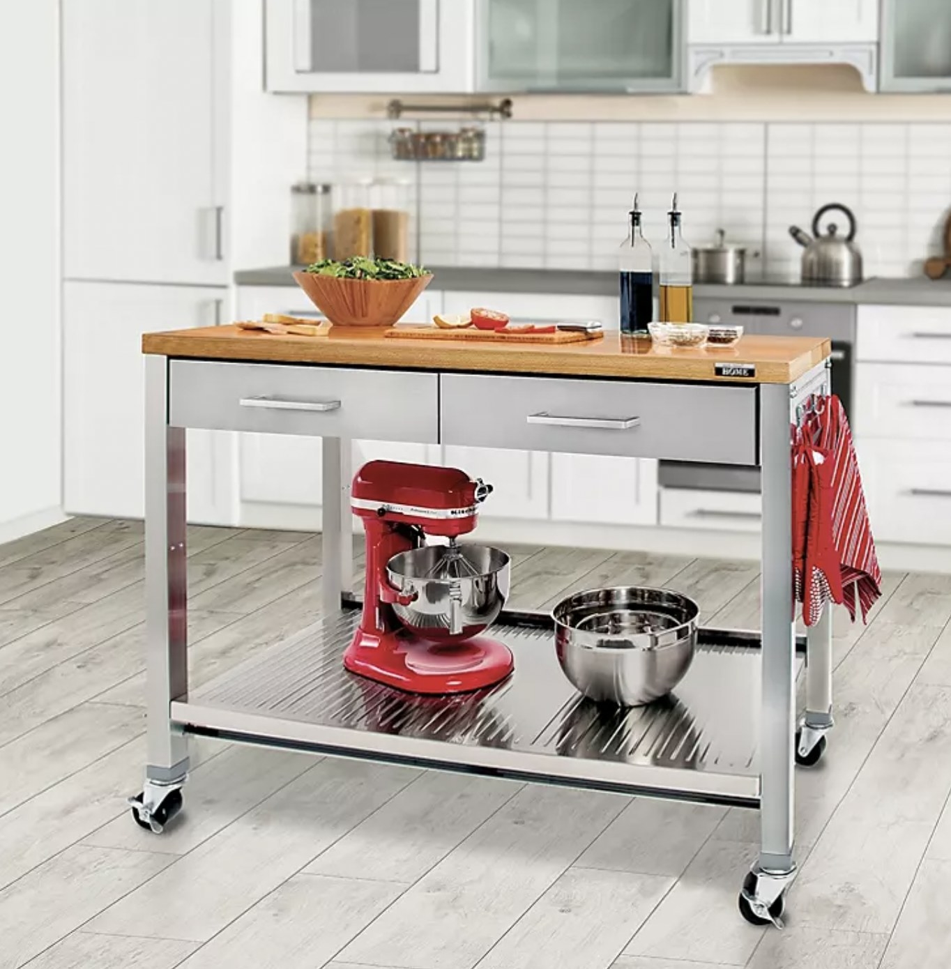 The cart on castor wheels in kitchen with Kitchen Aid and bowls on bottom shelf, towels and mitts on side hooks, and a salad being prepped on wooden surface
