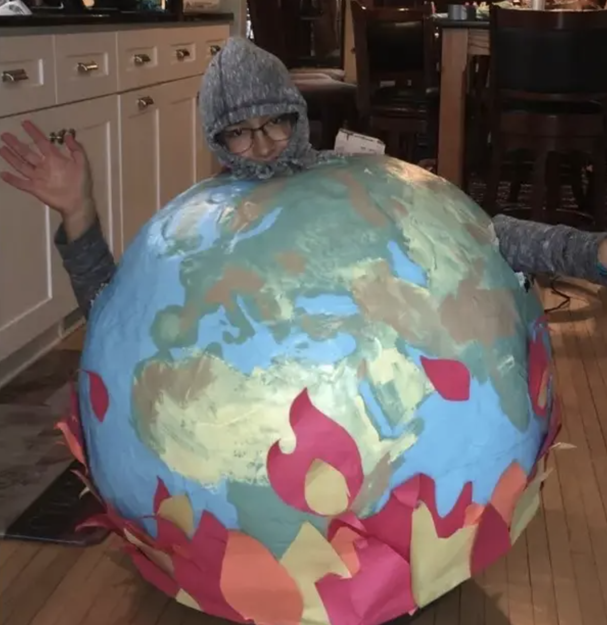 A person in a hoodie and wearing a huge globe costume with paper &quot;flames&quot; at the bottom of it
