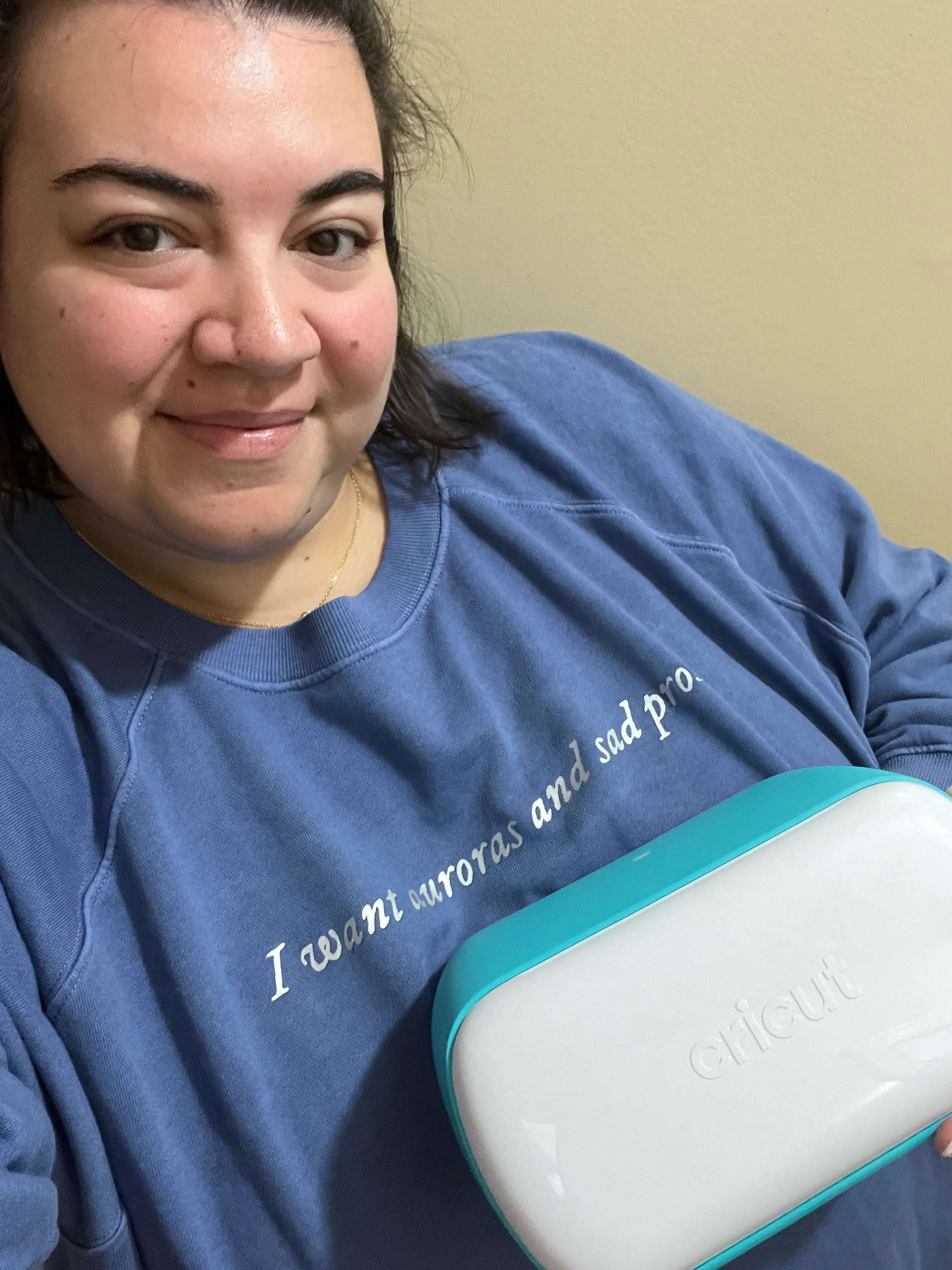 Bianca holding up a Cricut machine while wearing a sweater she made with it