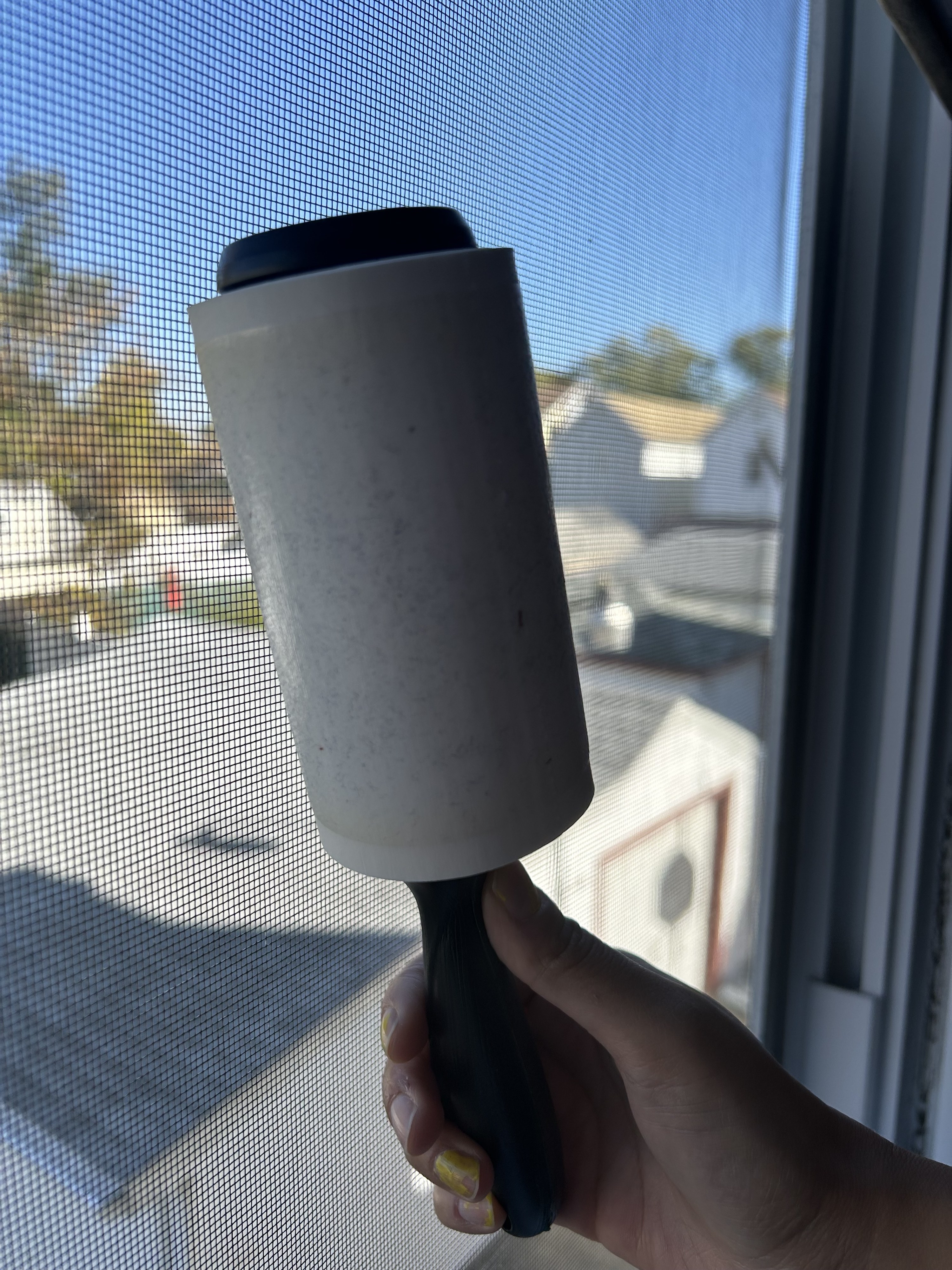 A person using a lint roller to clean a window screen