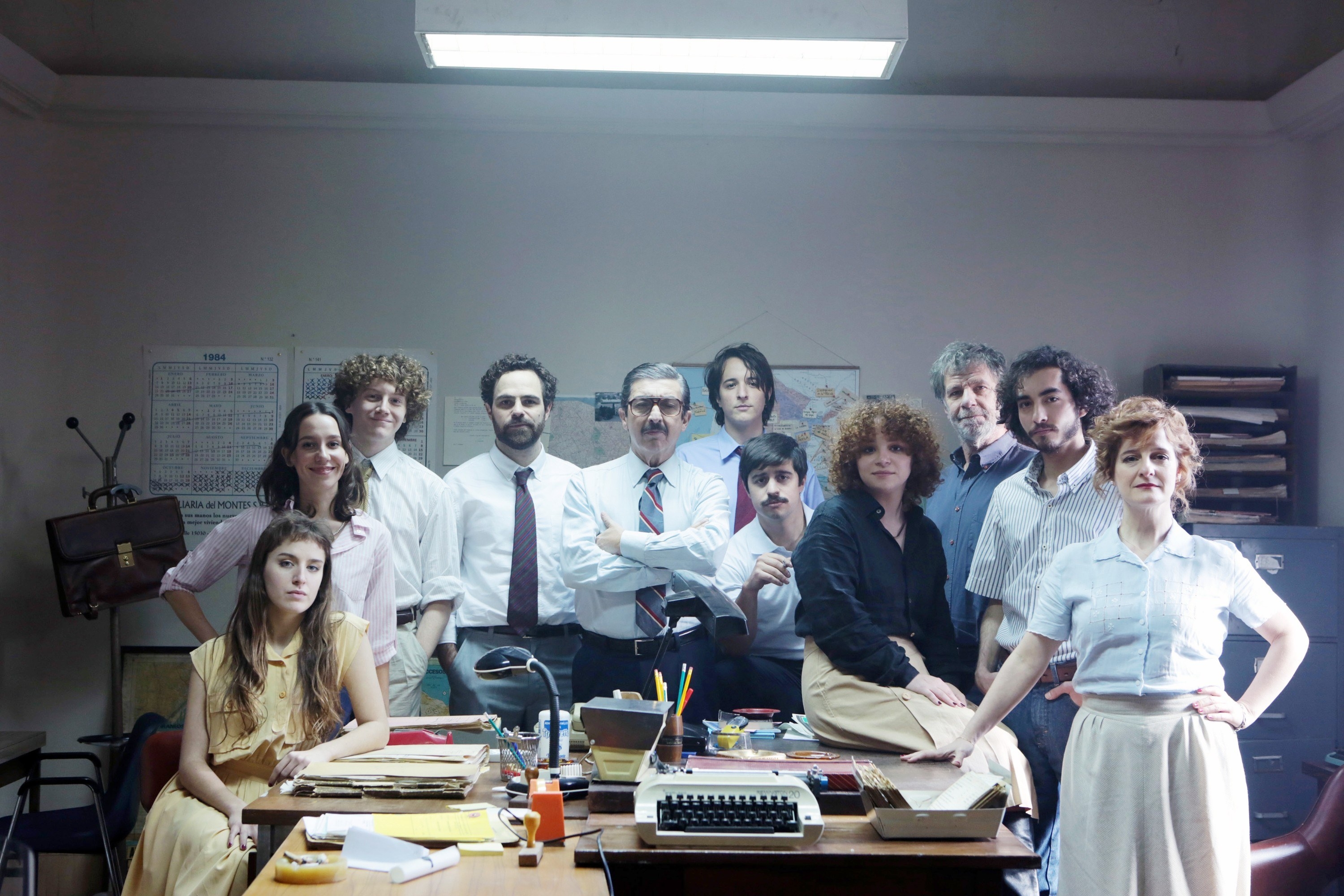 A group of people stand around a cluttered desk