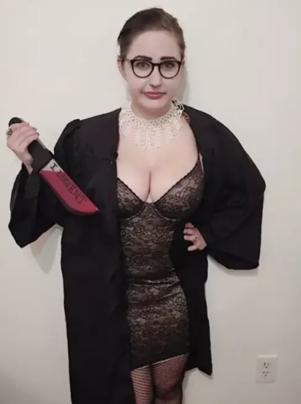 A woman in a black robe, short lacy dress, and fishnets, wearing glasses and holding a knife
