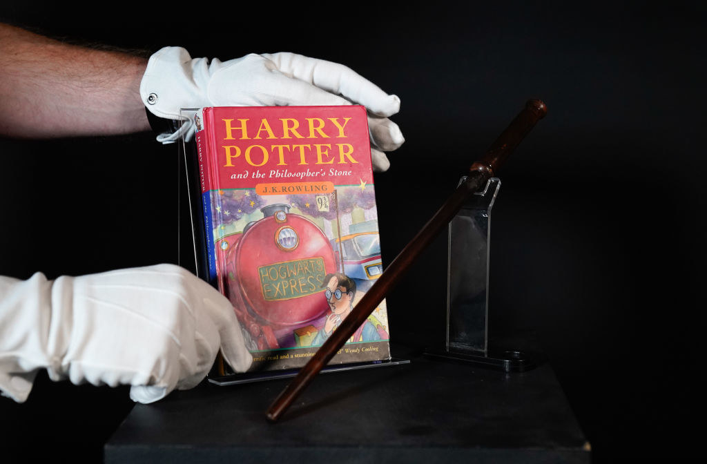 Someone with gloved hands carefully placing an edition of Harry Potter and the Philosopher&#x27;s Stone next to a wand