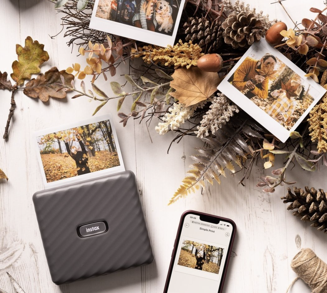 the printer connected to a phone printing a photo on the ground surrounded by fall decor