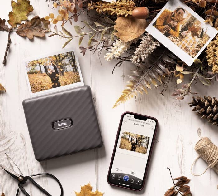 the printer connected to a phone printing a photo on the ground surrounded by fall decor