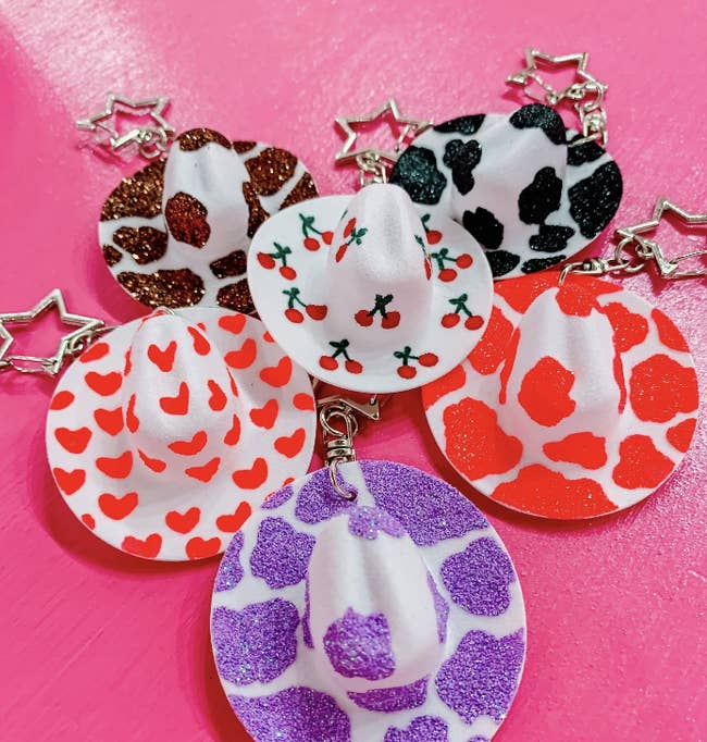 Mini cowboy hat keychains with cherry, heart, and multi-colored cow prints