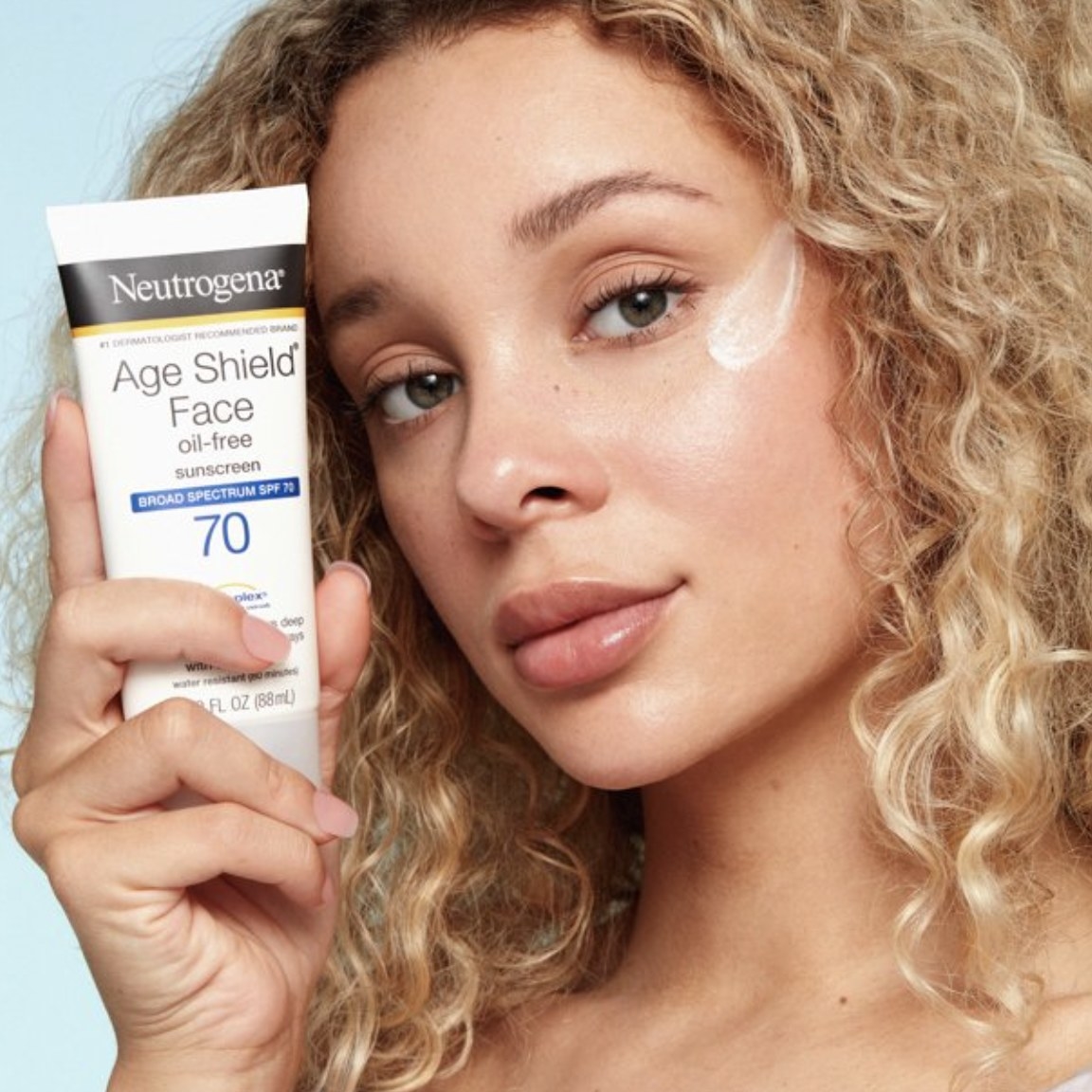 The model holds up the black, white and blue bottle that says &quot;Neutrogena Age Shield Face&quot;