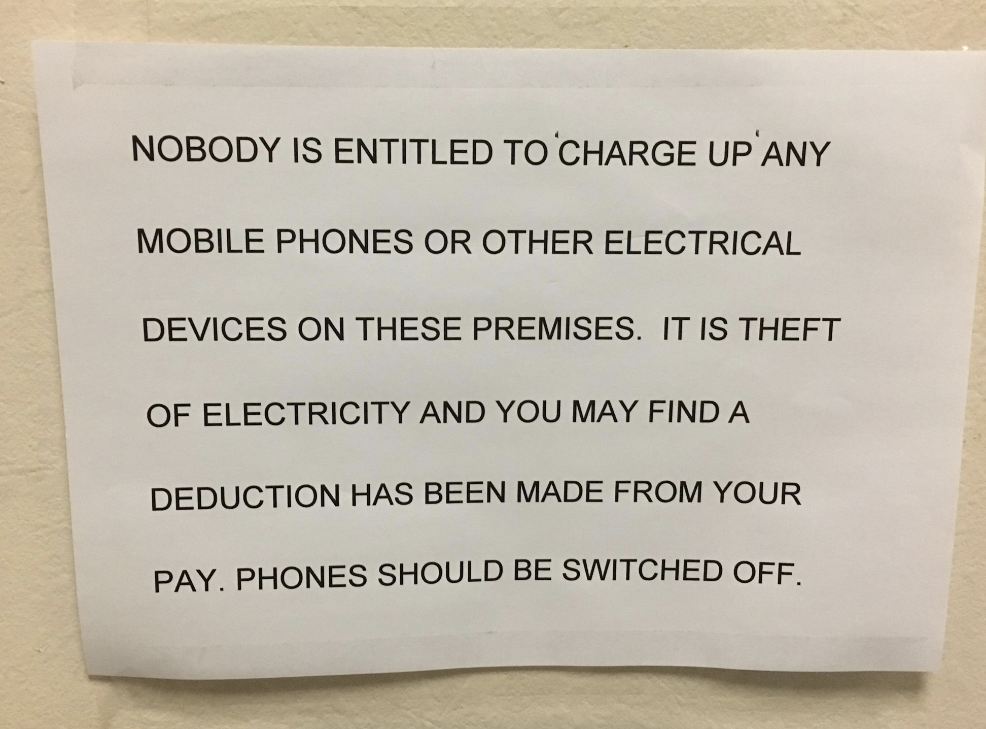 All-caps note on wall saying that no one can charge their electronic devices on the premises because it&#x27;s &quot;theft of electricity and you may find a deduction has been made from your pay&quot;
