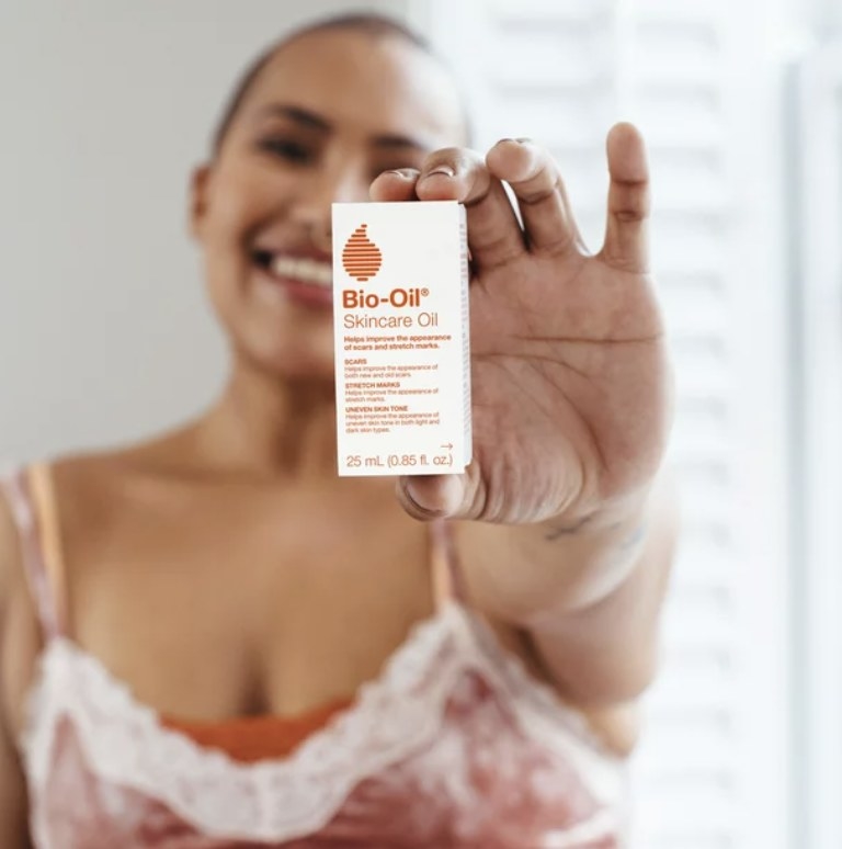 The model holds out the white box that says &quot;Bio-Oil SKincare Oil&quot; with an orange lined droplet