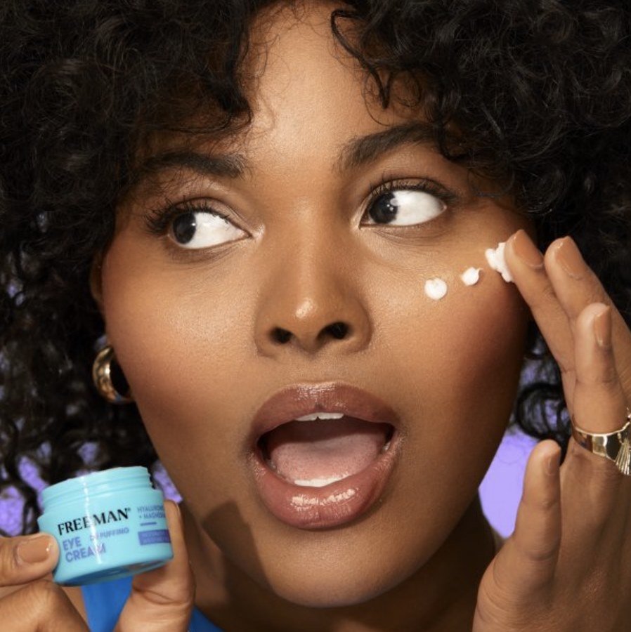 A model holds the little blue tub next to their face as they spread some under the eye on the right
