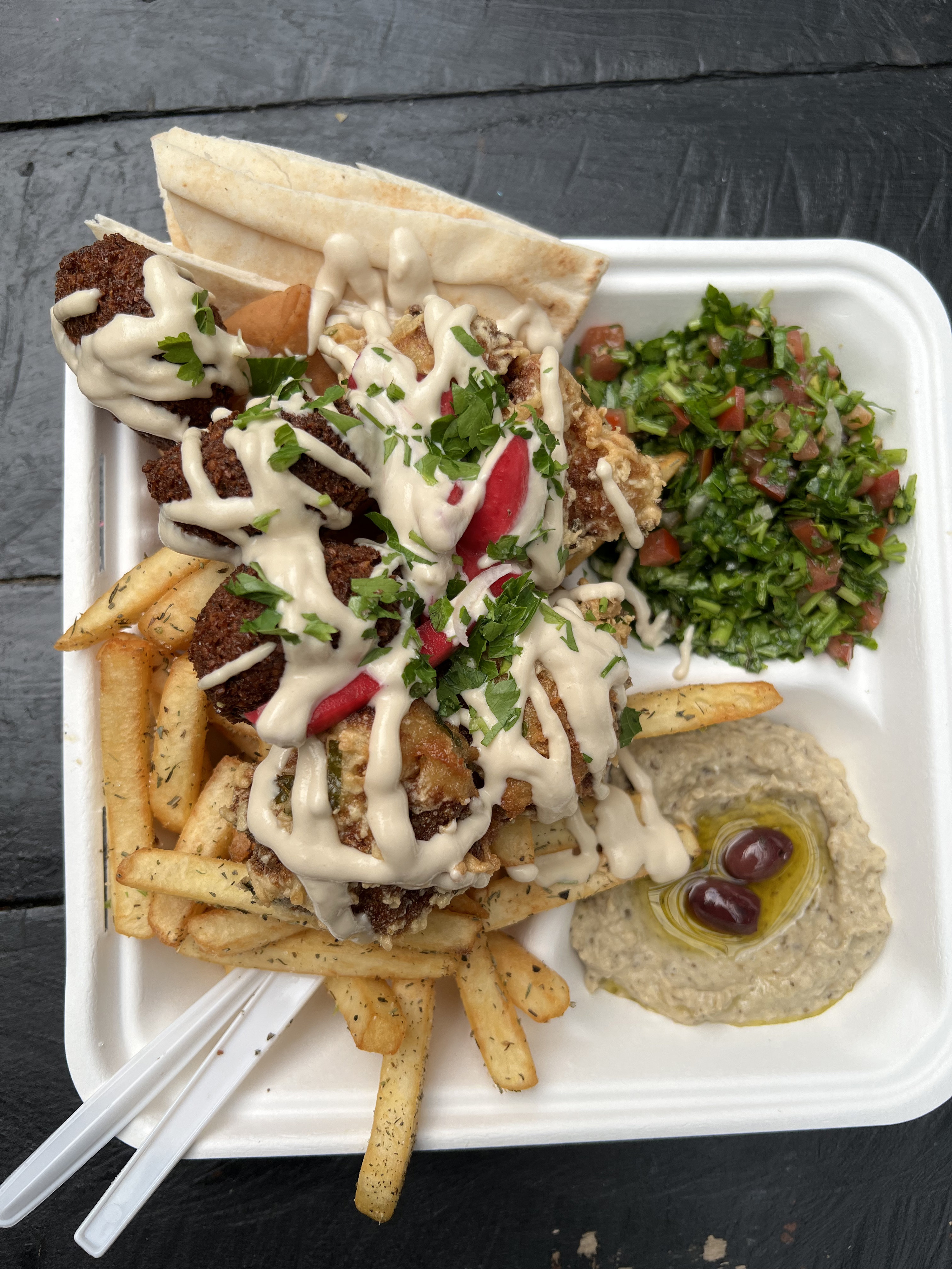 A takeout container filled with eggplant dip, tabouli, chips, falafel, cauliflower and pita bread