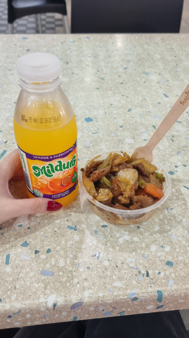 A bottle of juice and a small serving of stir-fry in a takeout container