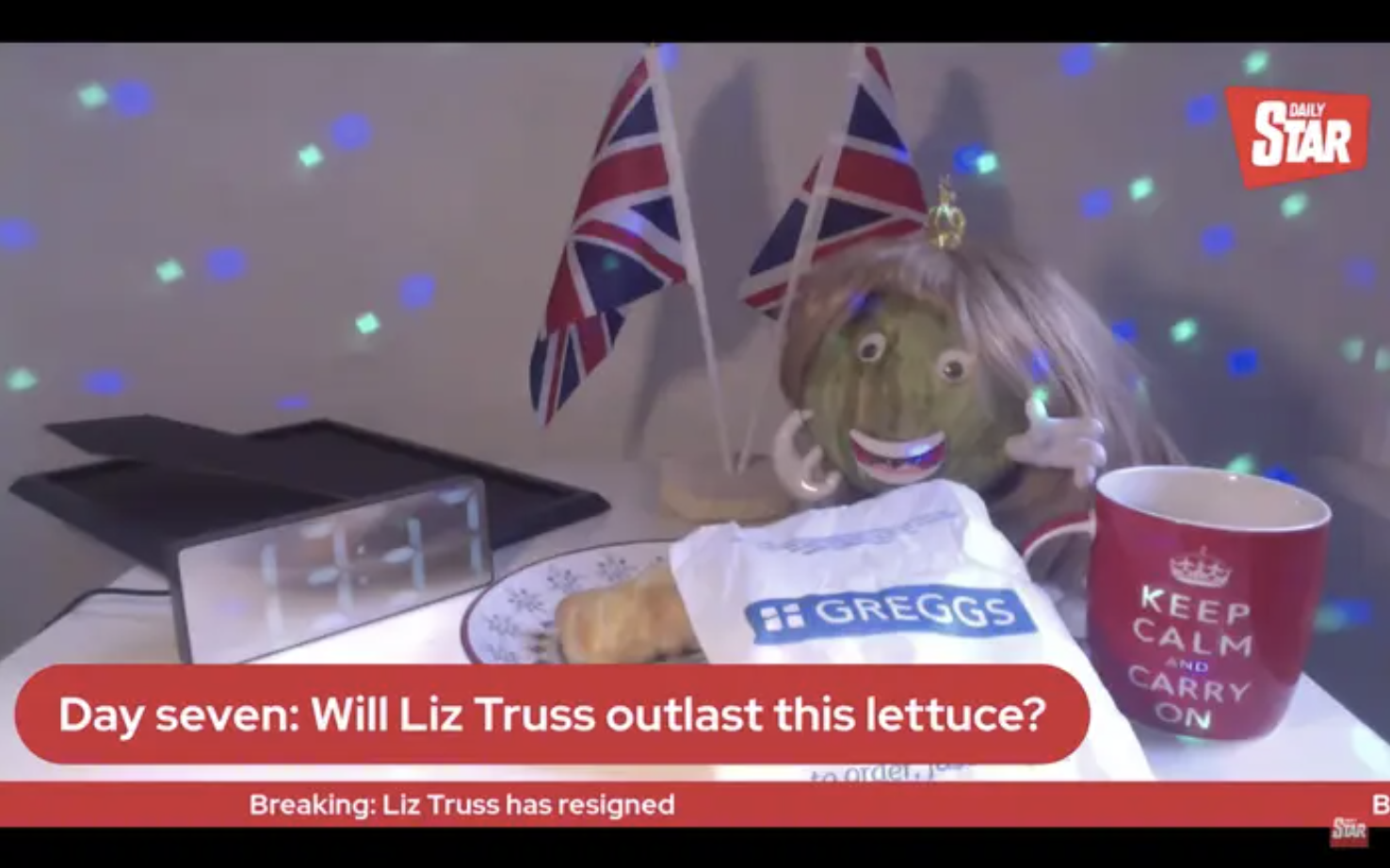 a screenshot of a youtube video featuring a head of lettuce with a smile and googley eyes and a wig, next to union jack flags and a keep calm and carry on. the text at the bottom reads &quot;day seven: will liz truss outlast this lettuce?&quot;