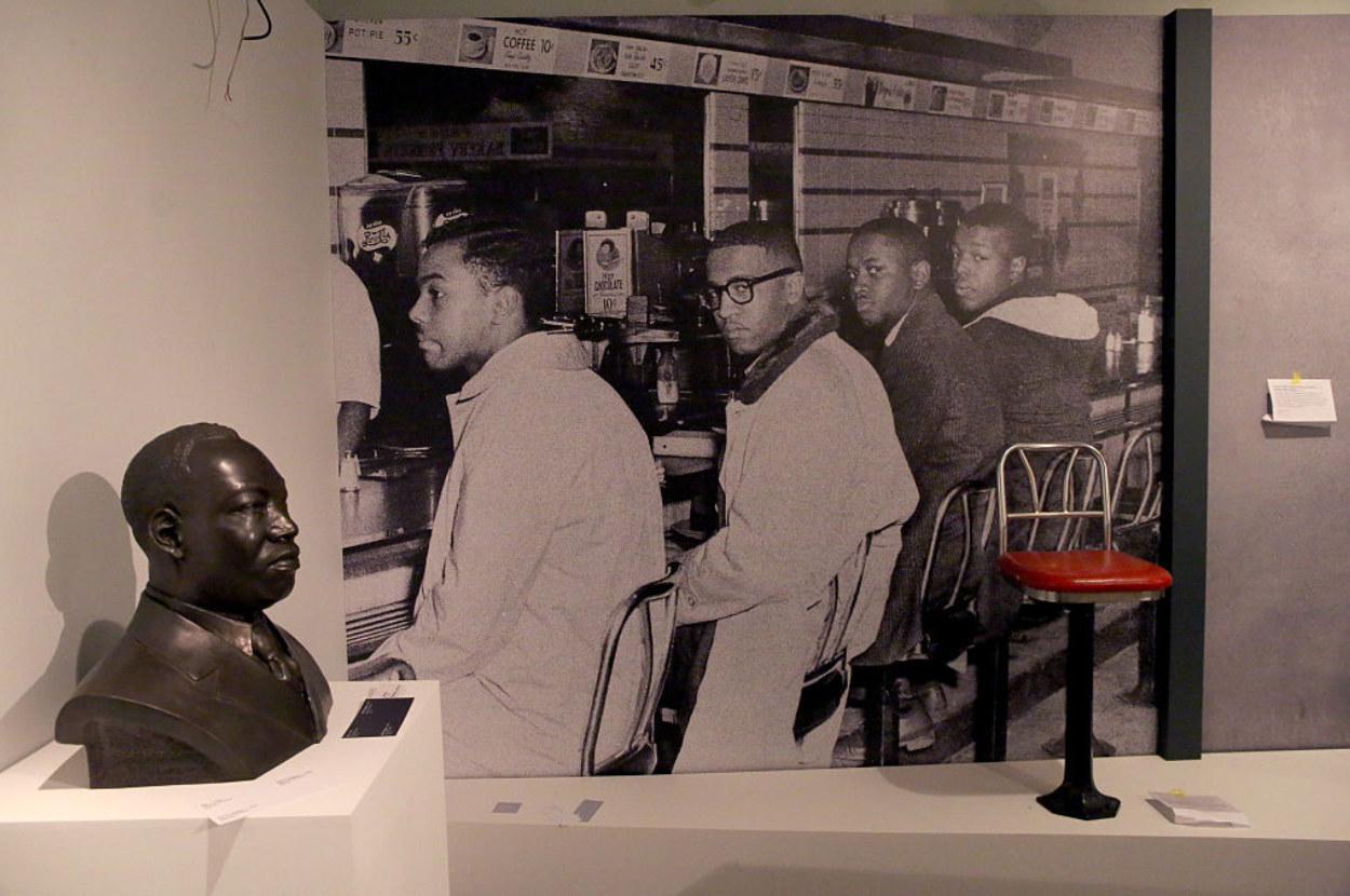 four black men sitting at counter and turning their heads towards the camera