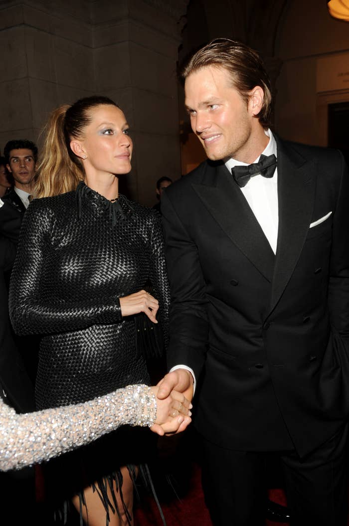 Giselle standing next to Tom as he shakes hands with someone at an event