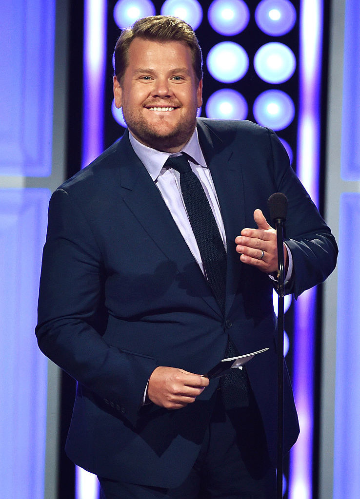 Smiling James in a suit at a microphone onstage