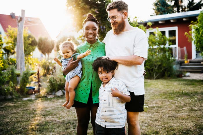 A portrait of a mixed race couple standing outdoors in their back garden with their two young children