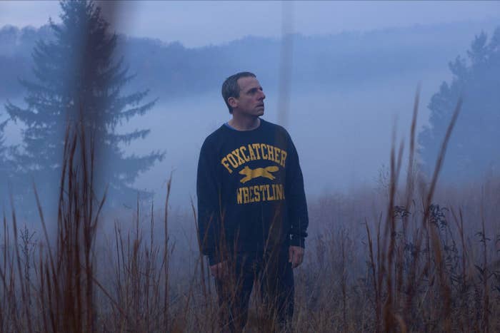 An older man in a blue wrestling sweatshirt stands in a foggy field