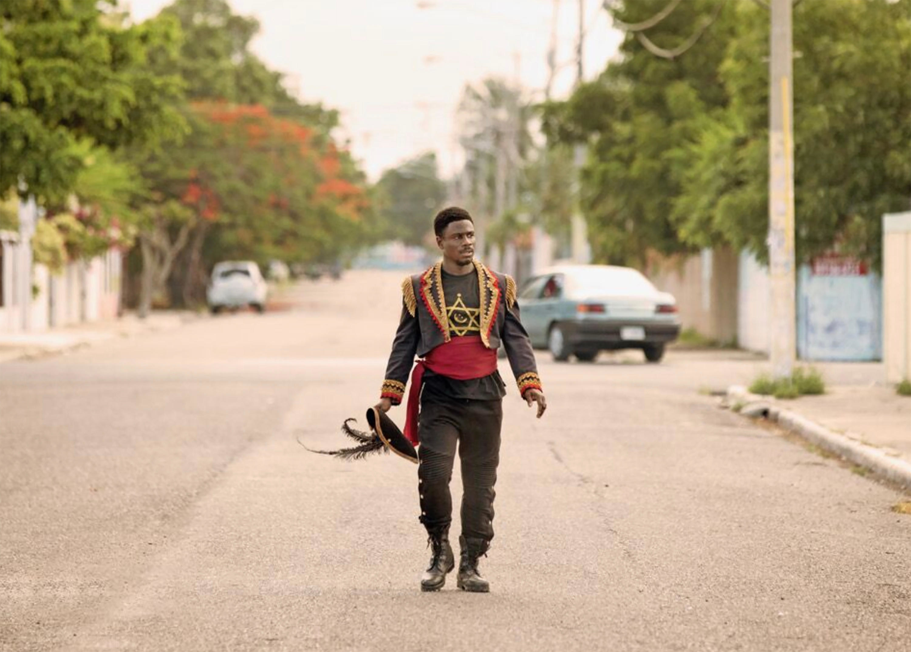 A Black man in ornate clothes walks down an empty street