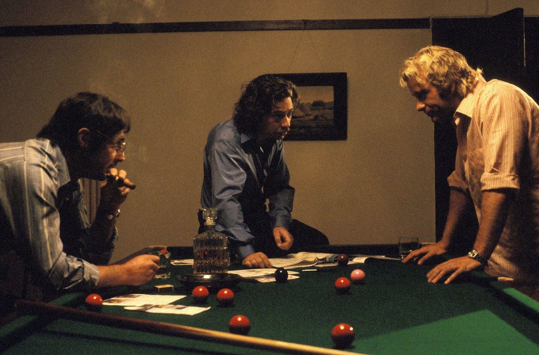 Three middle-aged fugitives discuss their next criminal move atop a pool table