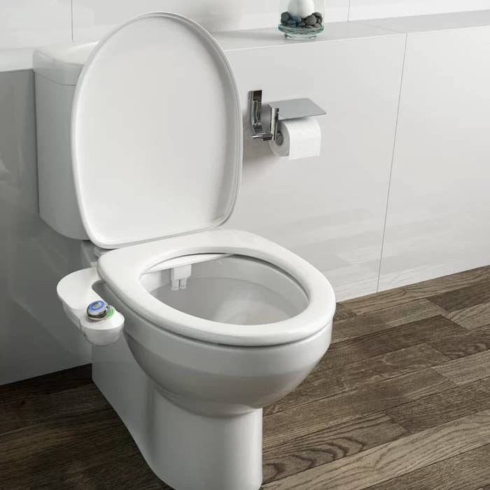 a toilet with an attached bidet set next to a mounted toilet paper roll