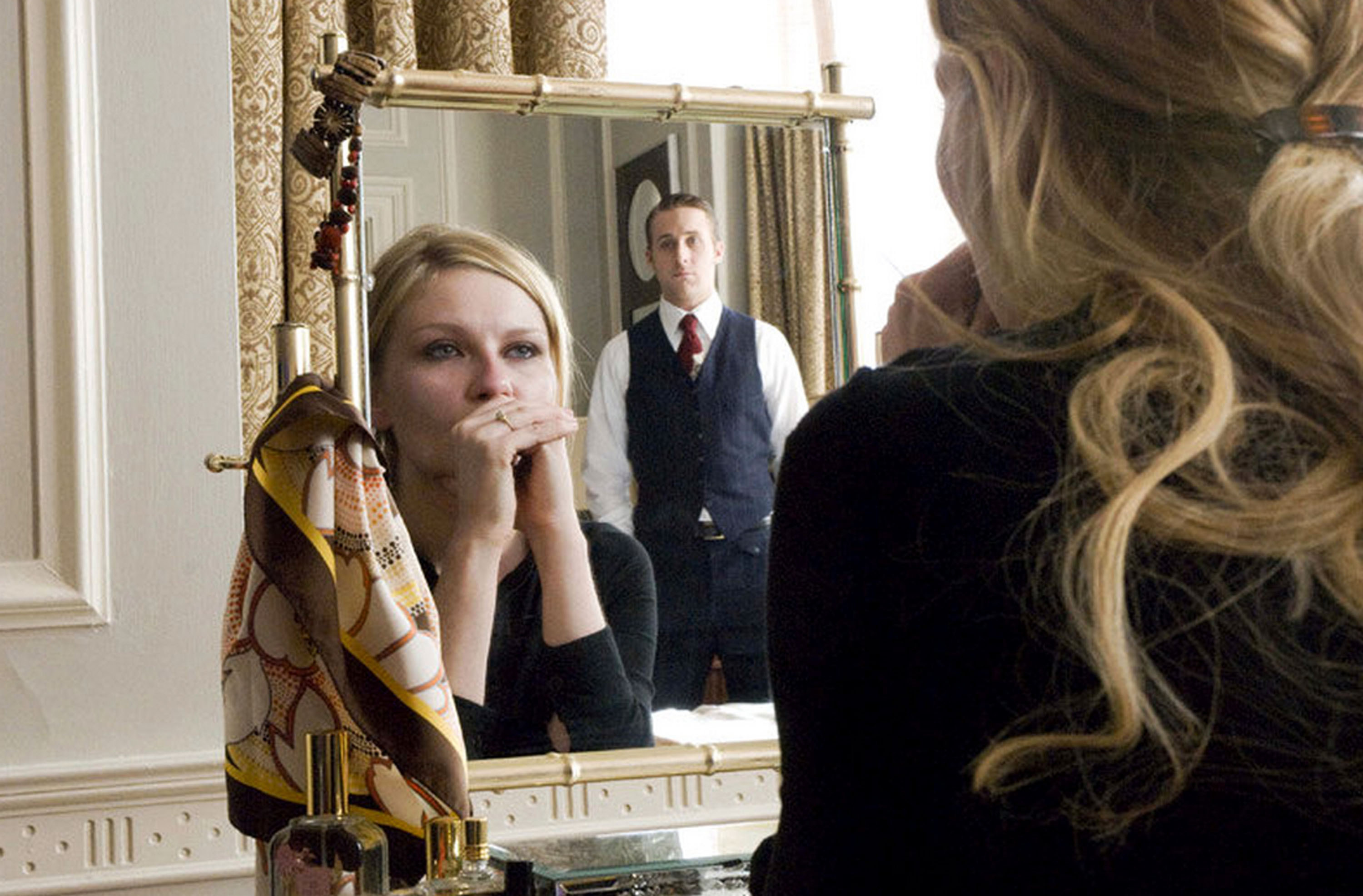 A man stares coldly at a blonde woman near her mirror