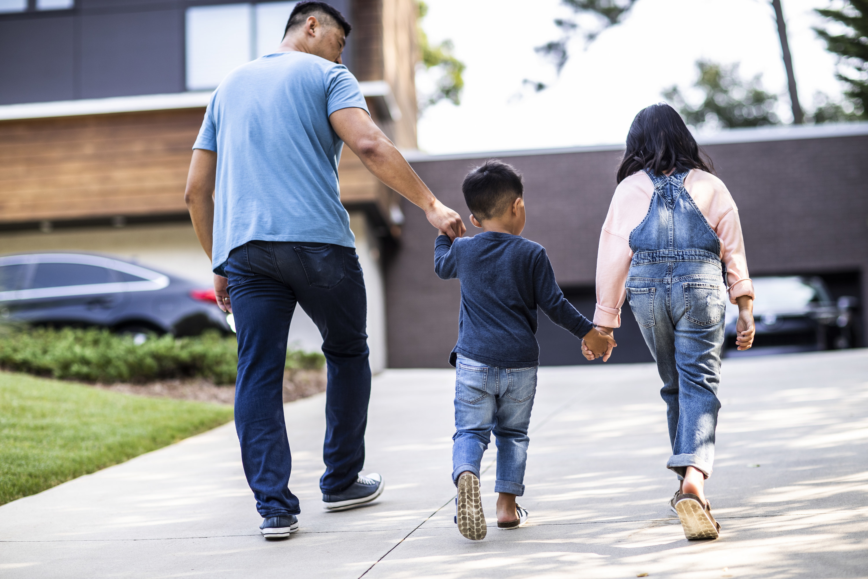 Father and children walking up driveway to modern home