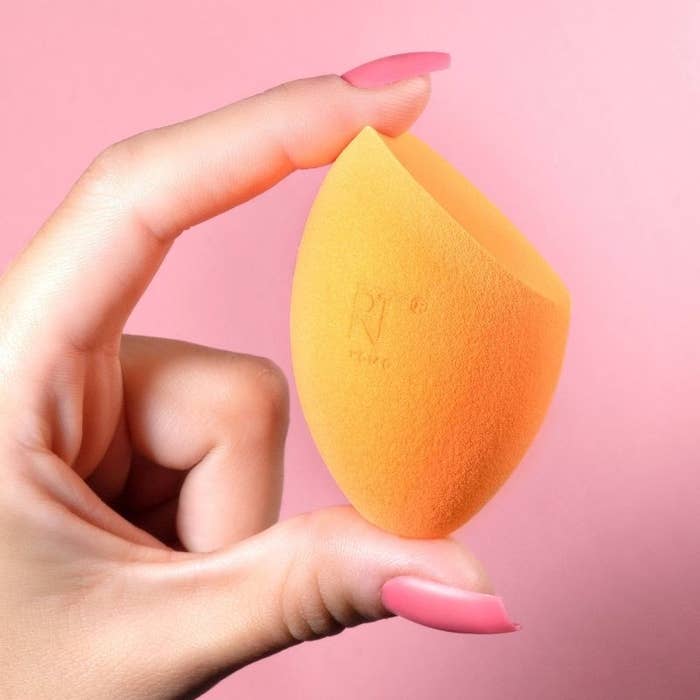 A person with a pink manicure holding an orange makeup sponge