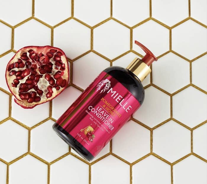 A bottle of leave-in conditioner with a sliced pomegranate