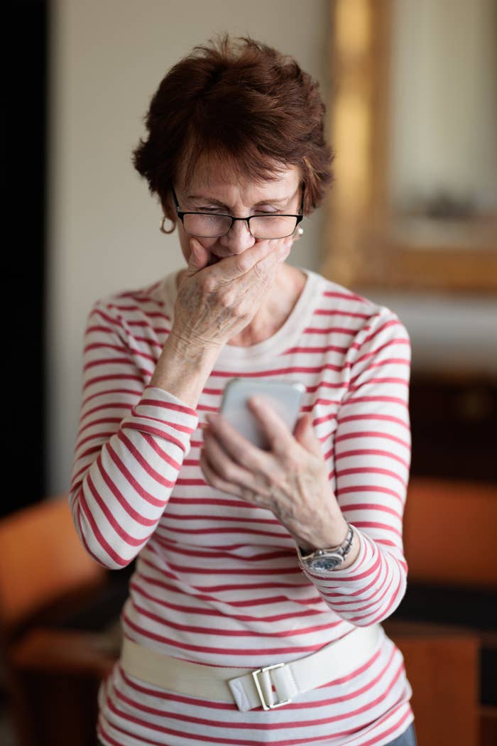 Older person covering mouth while looking at phone