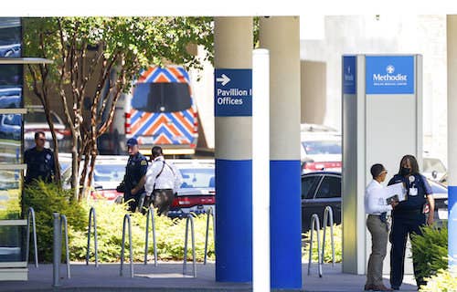 Police standing outside a hospital with police cars parked