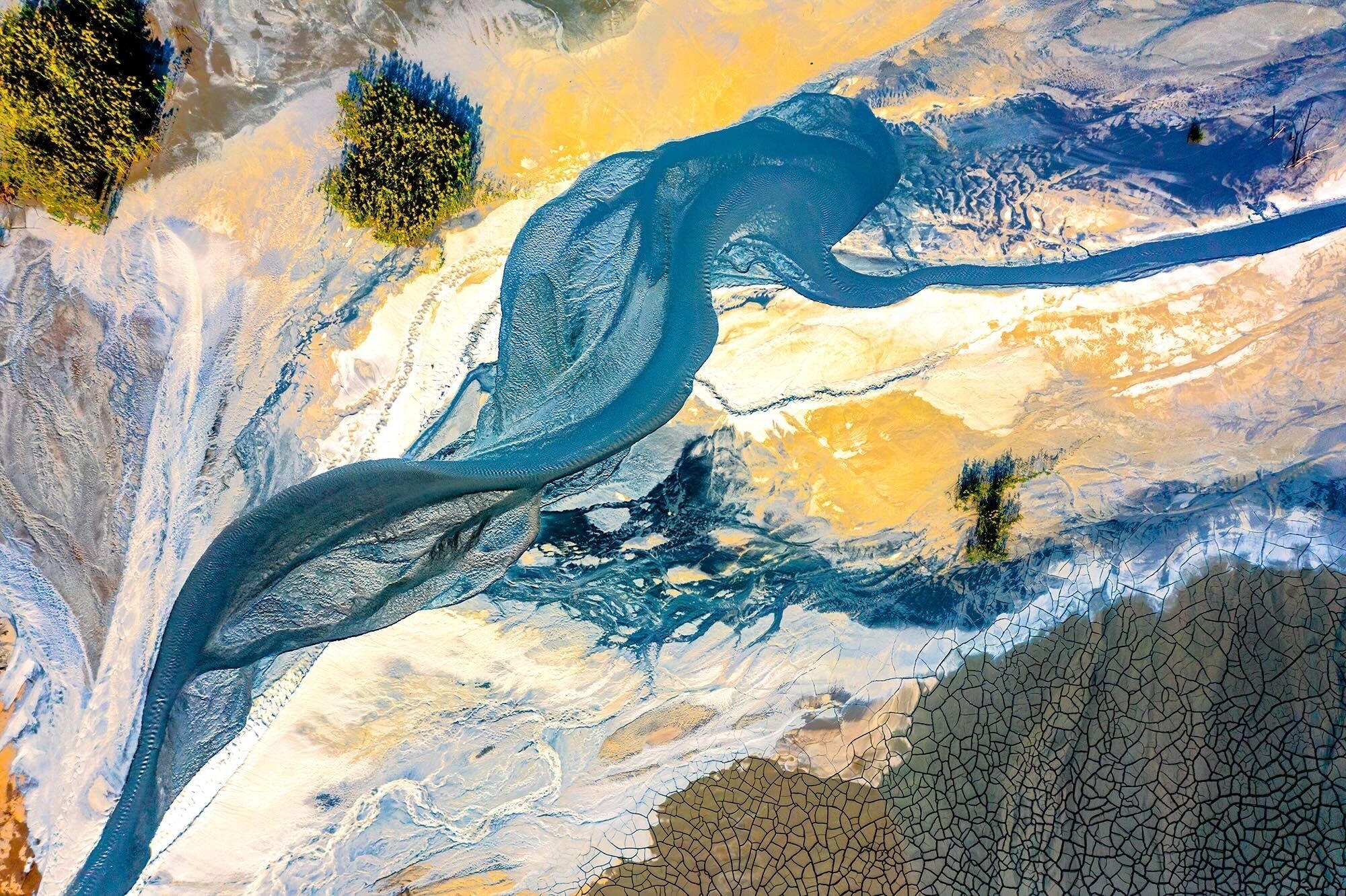 An aerial shot of a mine tailing dam in china; looks like a blue and yellow and white watercolor river