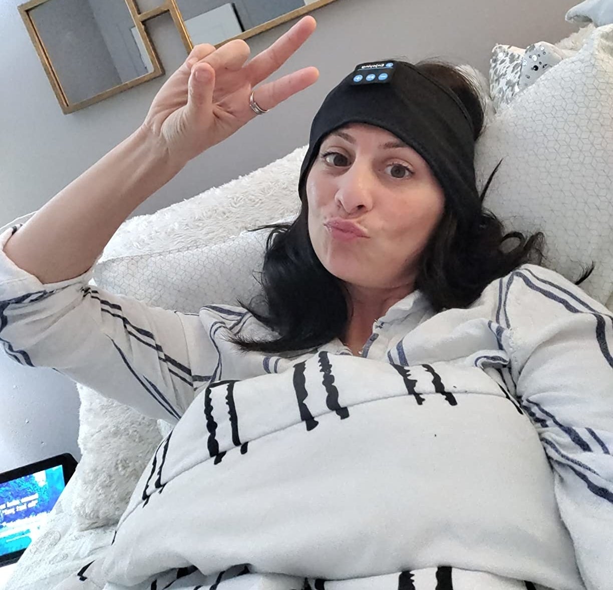 Reviewer in bed with black headband on giving peace sign with right hand