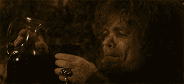 Tyrion Lannister smirking while holding a glass filled to the rim with wine