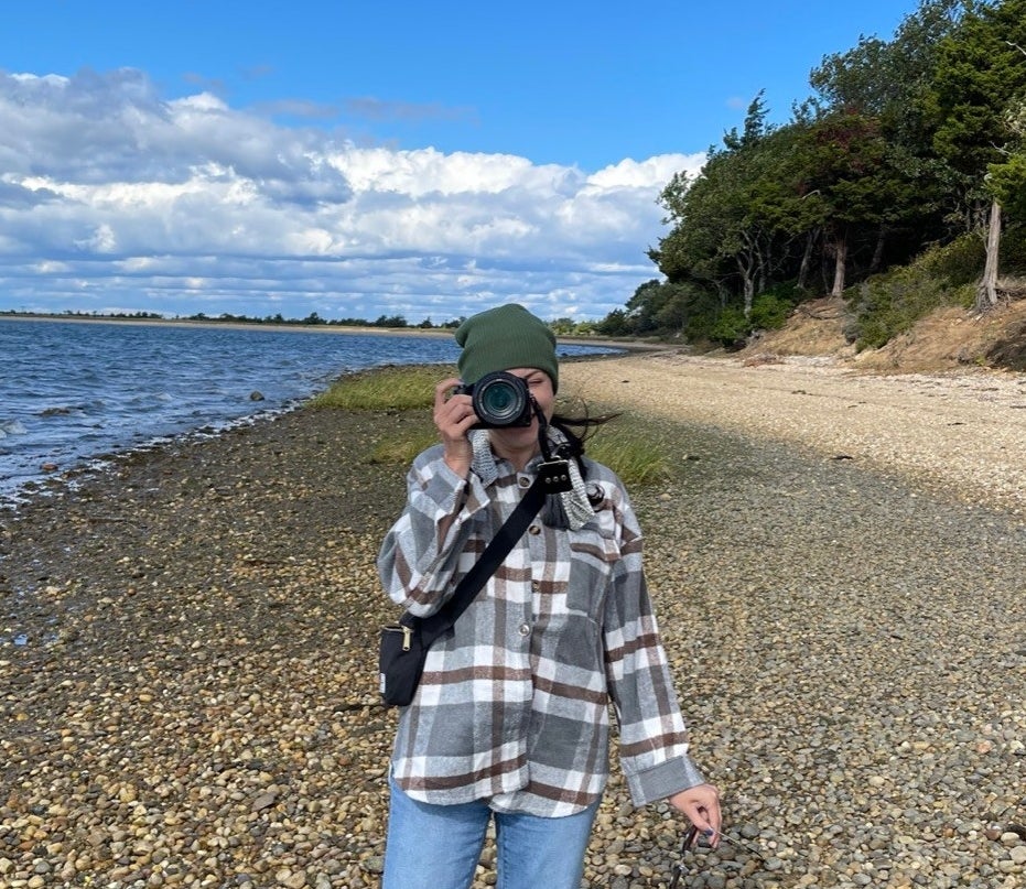 Reviewer on beach with camera at eye wearing the grey flannel shacket