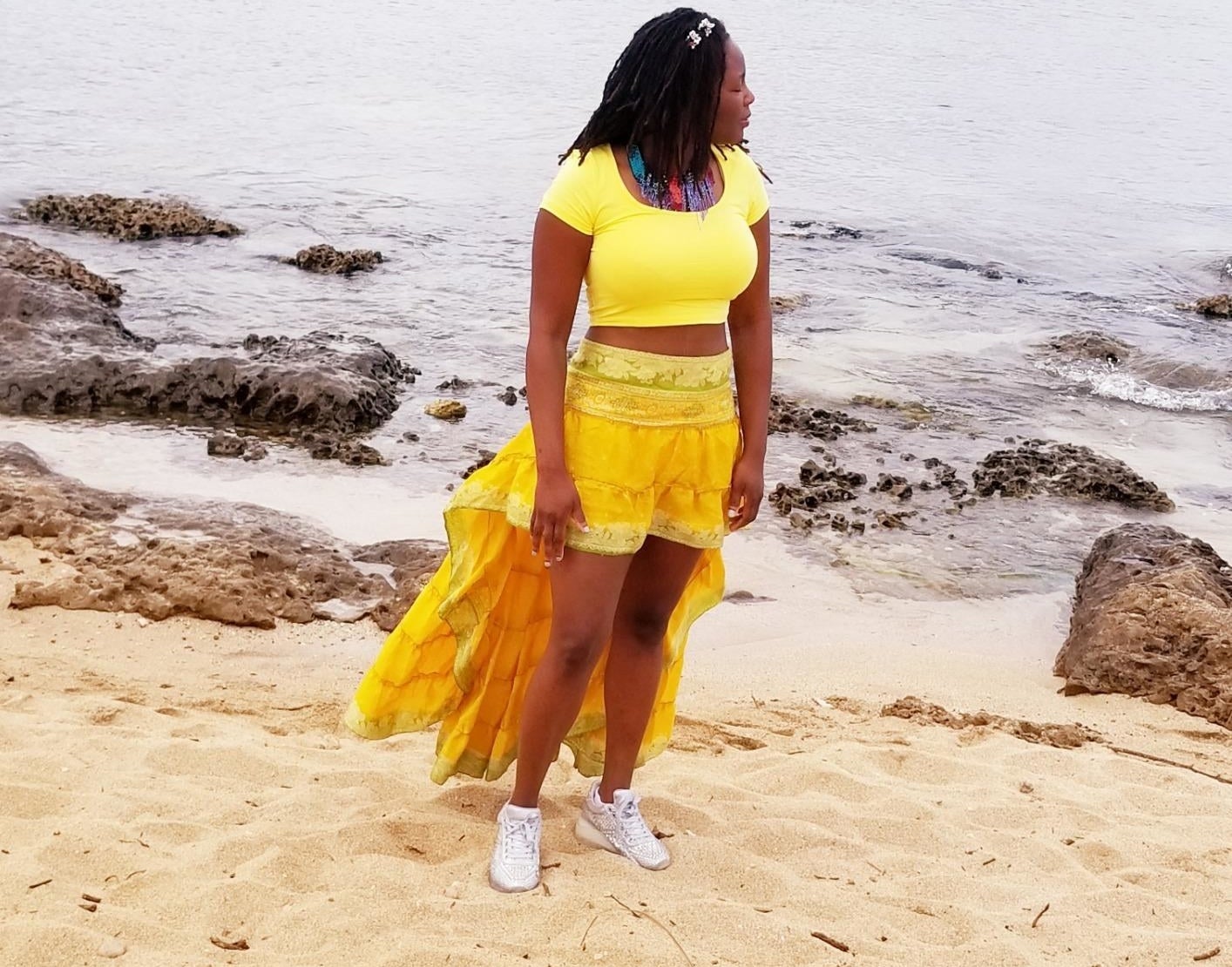 Reviewer standing on beach wearing the yellow crop top with high waisted high-low skort