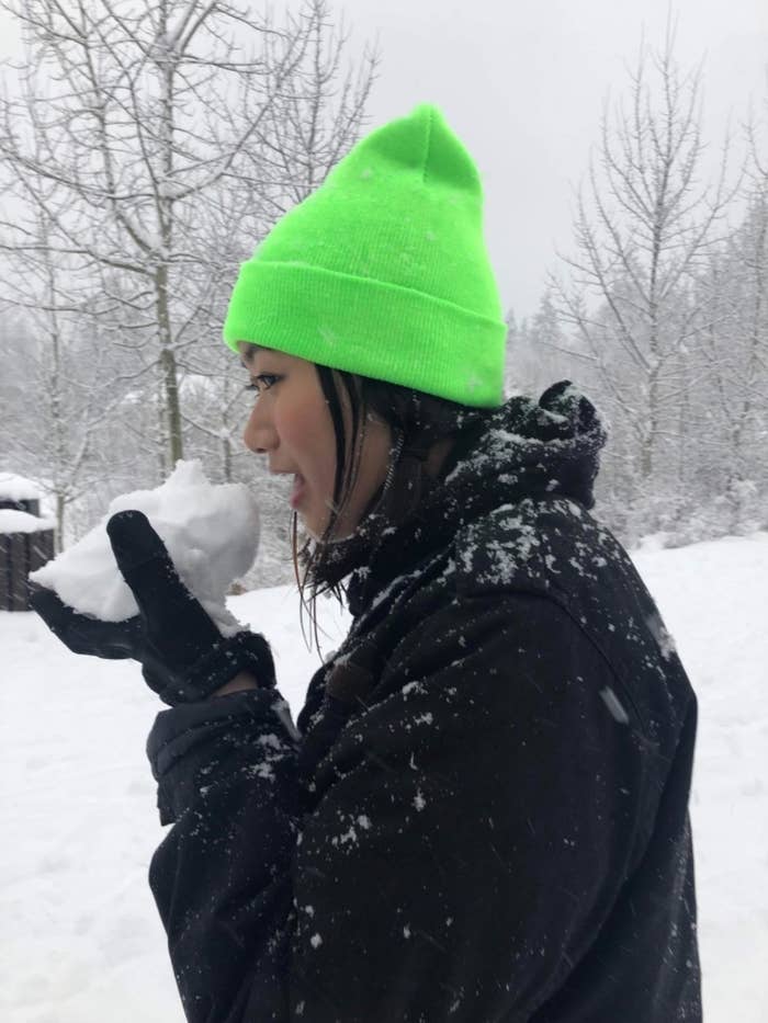 Reviewer in a blizzard holding a snowball up to face wearing the bright green beanie
