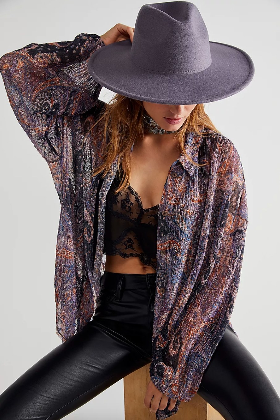 a model wearing the grey felt hat, a patterned shirt, black bralette, and black leather pants