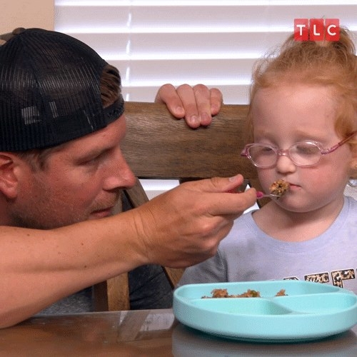 dad holding a forkful of food in front of a kid&#x27;s closed mouth