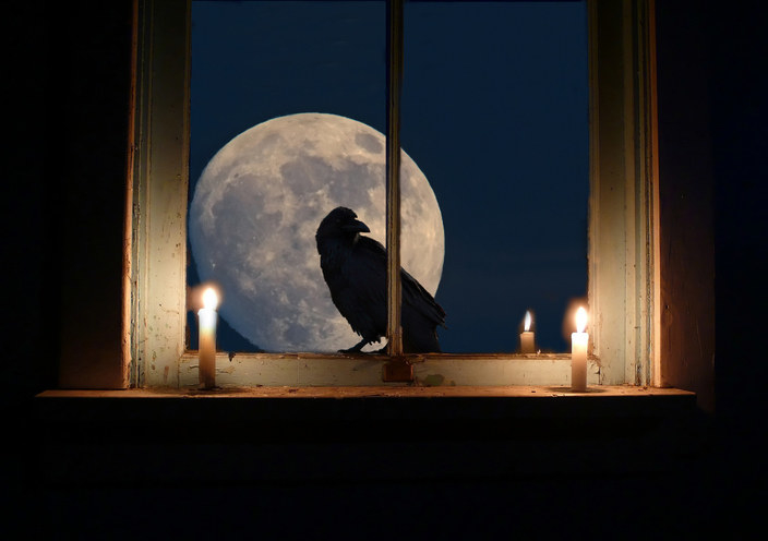 A raven sits outside the window with the full moon behind in a spooky night scene with candles.