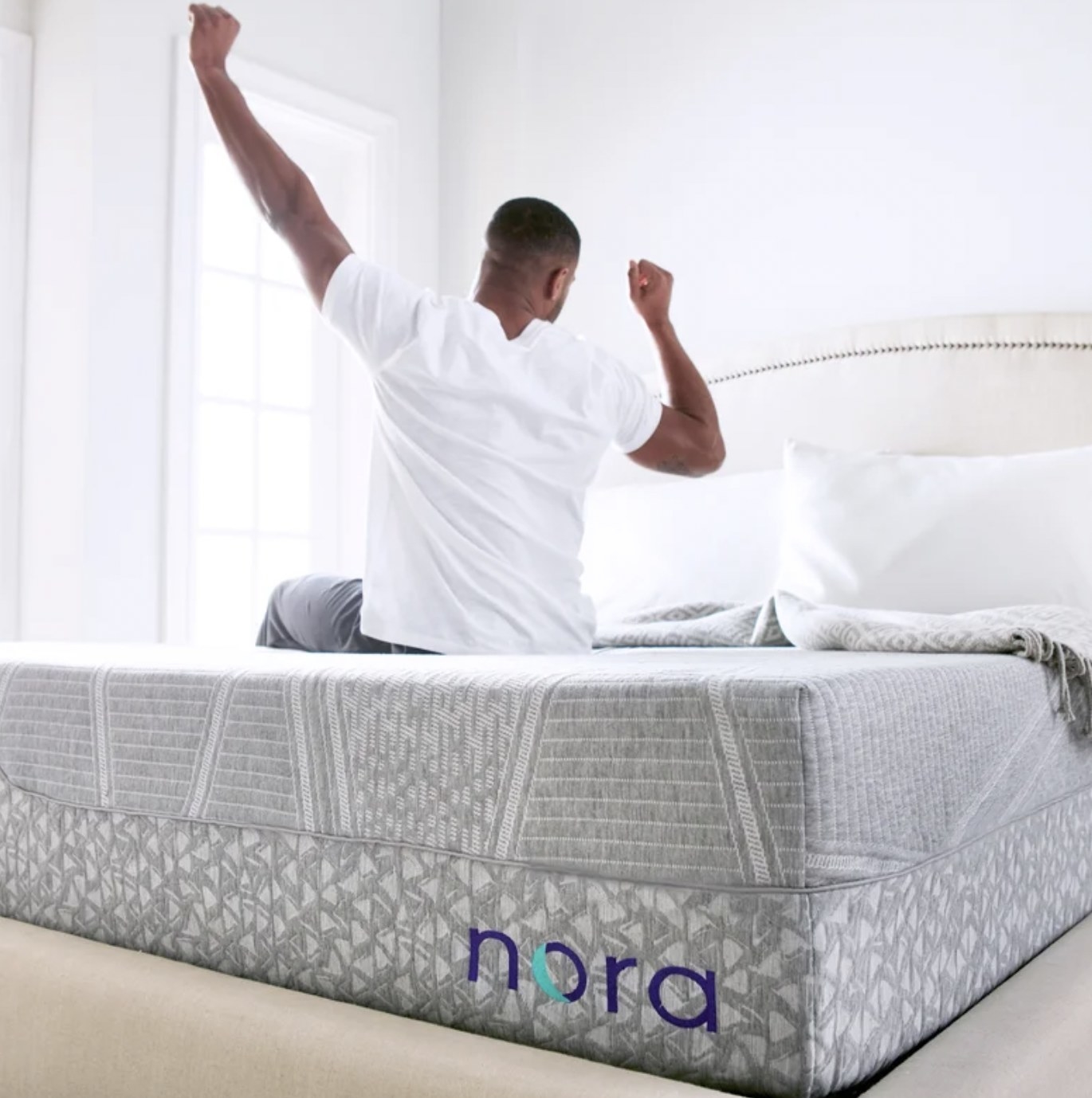 Person sitting on mattress and stretching arms above head
