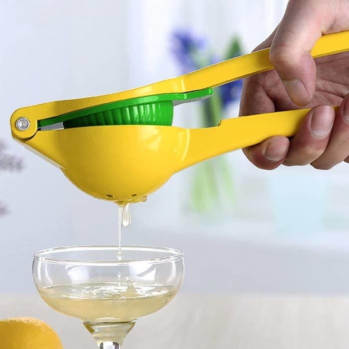 a person using the citrus squeezer to squeeze juice into a coupe