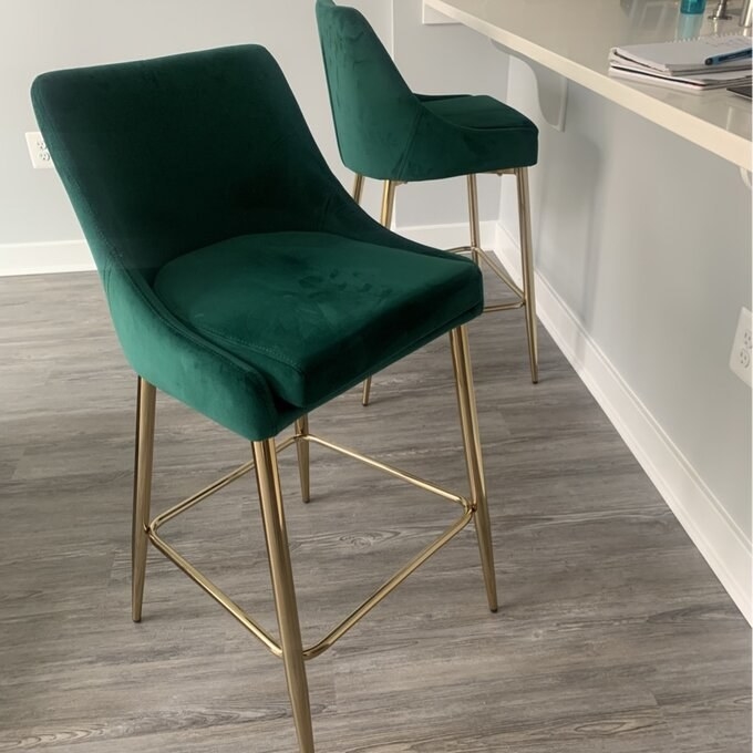 Two green upholstered barstools with gold legs