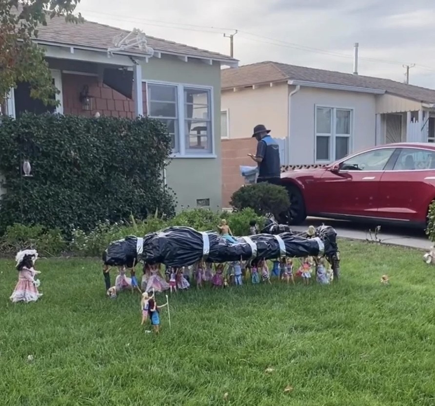 around 20 dolls in the yard propped up to hold a person in a trash bag