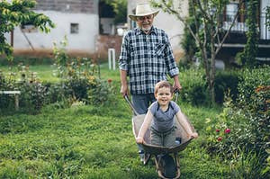 A grandparent is pushing their grandchild around in a wheelbarrow 