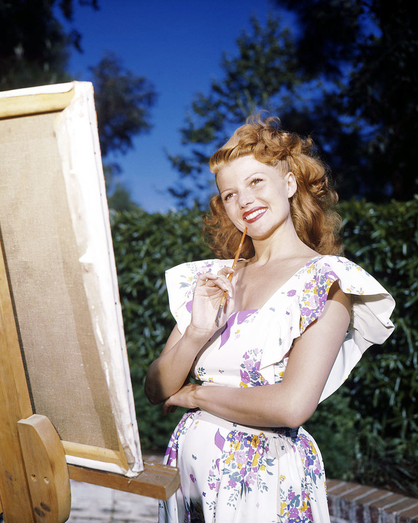 Rita posing behind an art canvas with a paint brush in hand