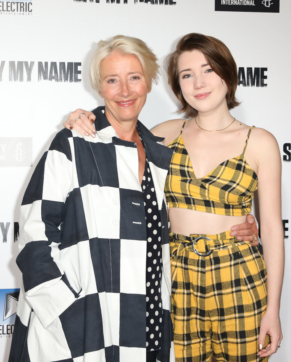 Emma in a checkered-print outfit and Gaia in plaid with their arms around each other on the red carpet