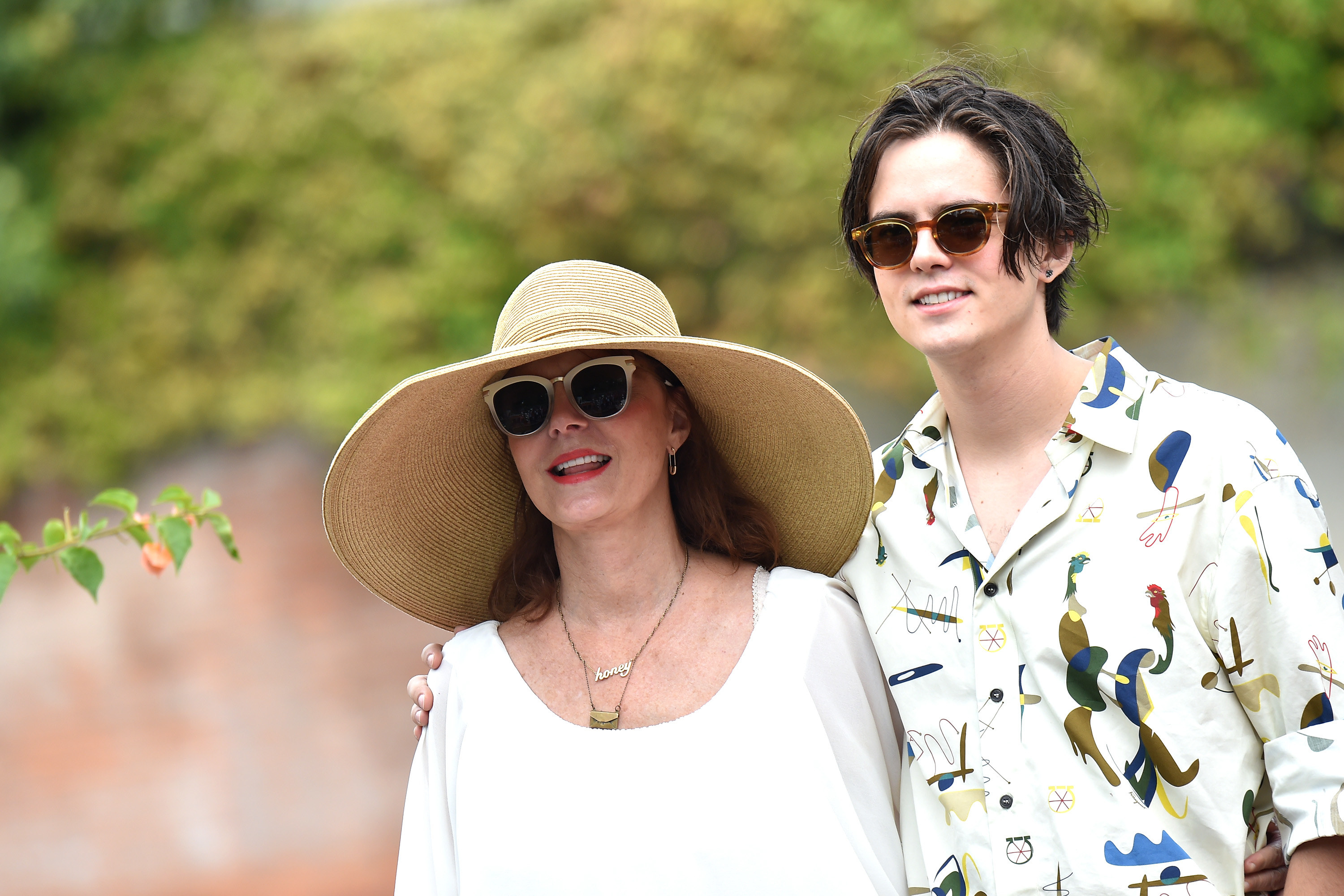 Susan in a wide-brimmed sun hat and Miles with his arm around her shoulders outdoors