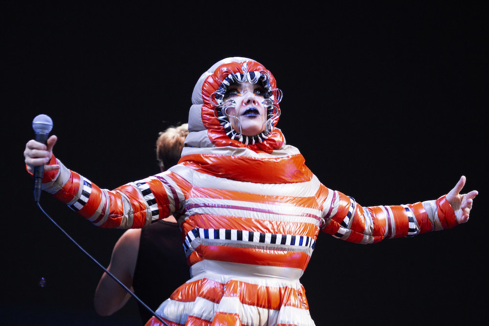 Björk performing in a puffy, full-body, multicolored outfit