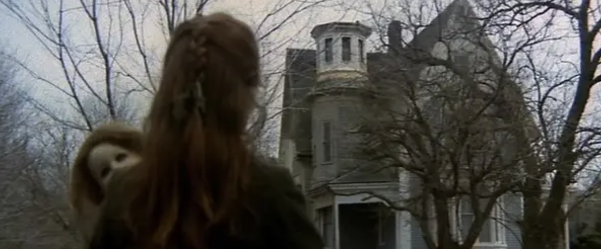 womans back to the camera as she looks at a creepy old house